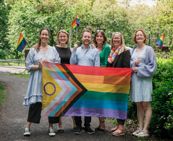Bilde av mennesker som holder et stort pride-flagg.